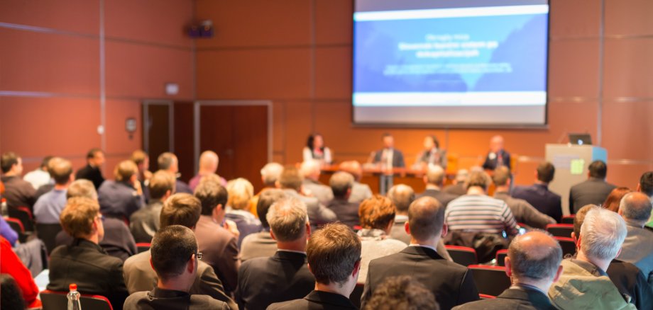 Publikum auf Konferenz mit Präsentation im Hintergrund