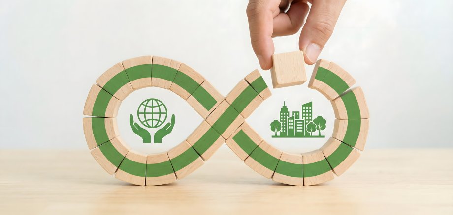 Konzept der Kreislaufwirtschaft Konzept der Kreislaufwirtschaft: Eine Hand formt eine Unendlichkeitsschleife mit Symbolen aus Holz für Ökostädte und die Welt.