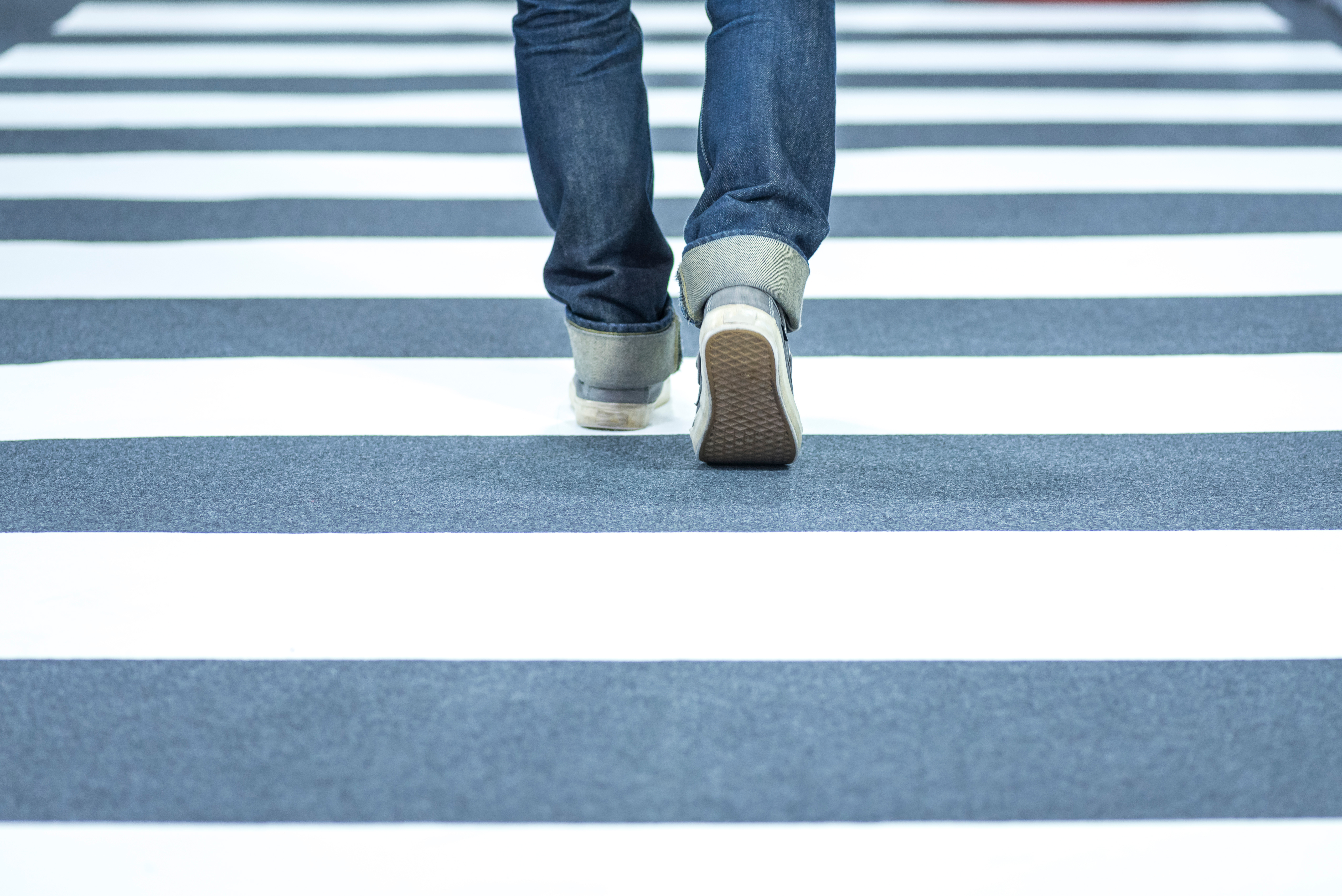 Zebrastreifen Mann in Jeans, der einen Zebrastreifen überquert.